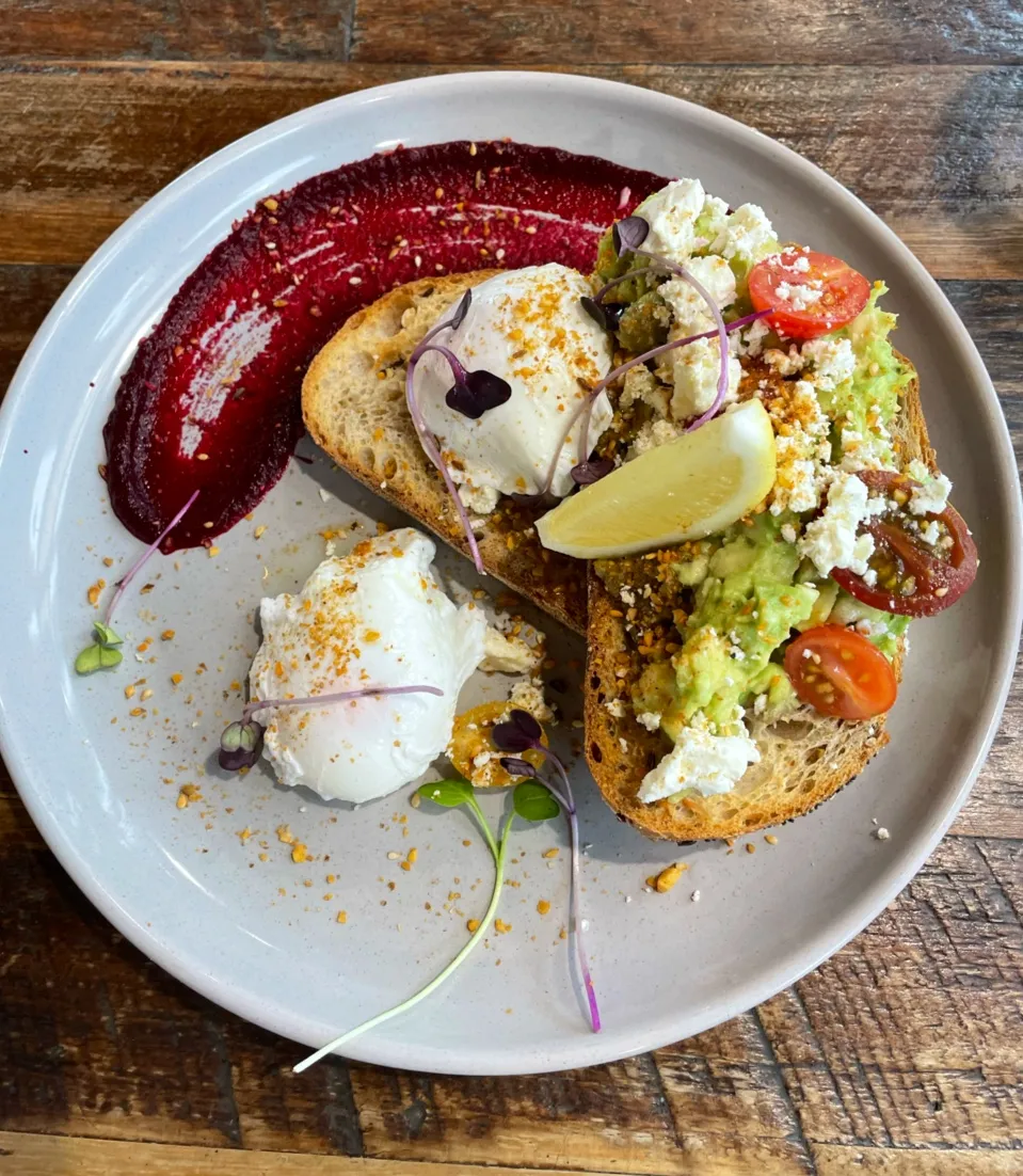 Breakfast plate with avocado toast, poached egg, beetroot and feta on ceramic dish