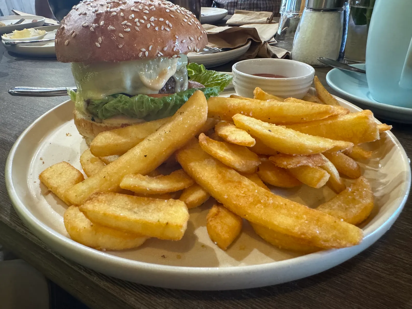 Cheeseburger with thick-cut chips and tomato sauce on a white plate