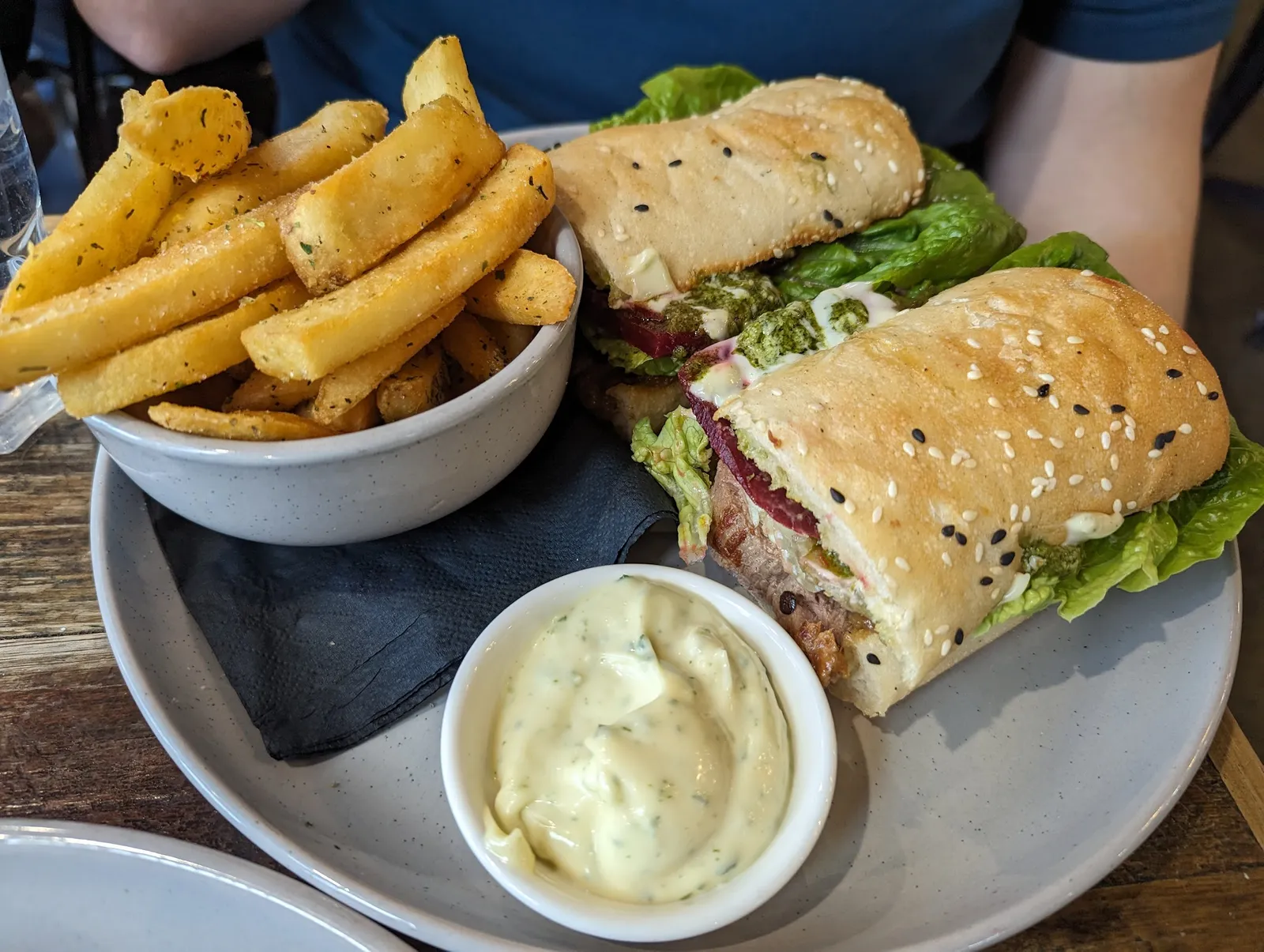 Sesame focaccia sandwich halved with chips and aioli on a dark plate