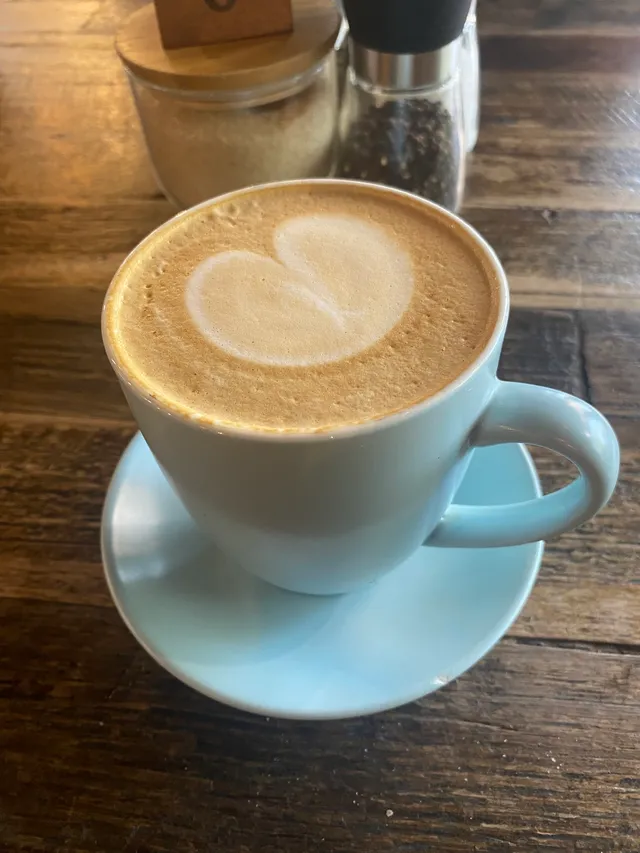 Flat white with heart milk art in pale blue cup on timber table