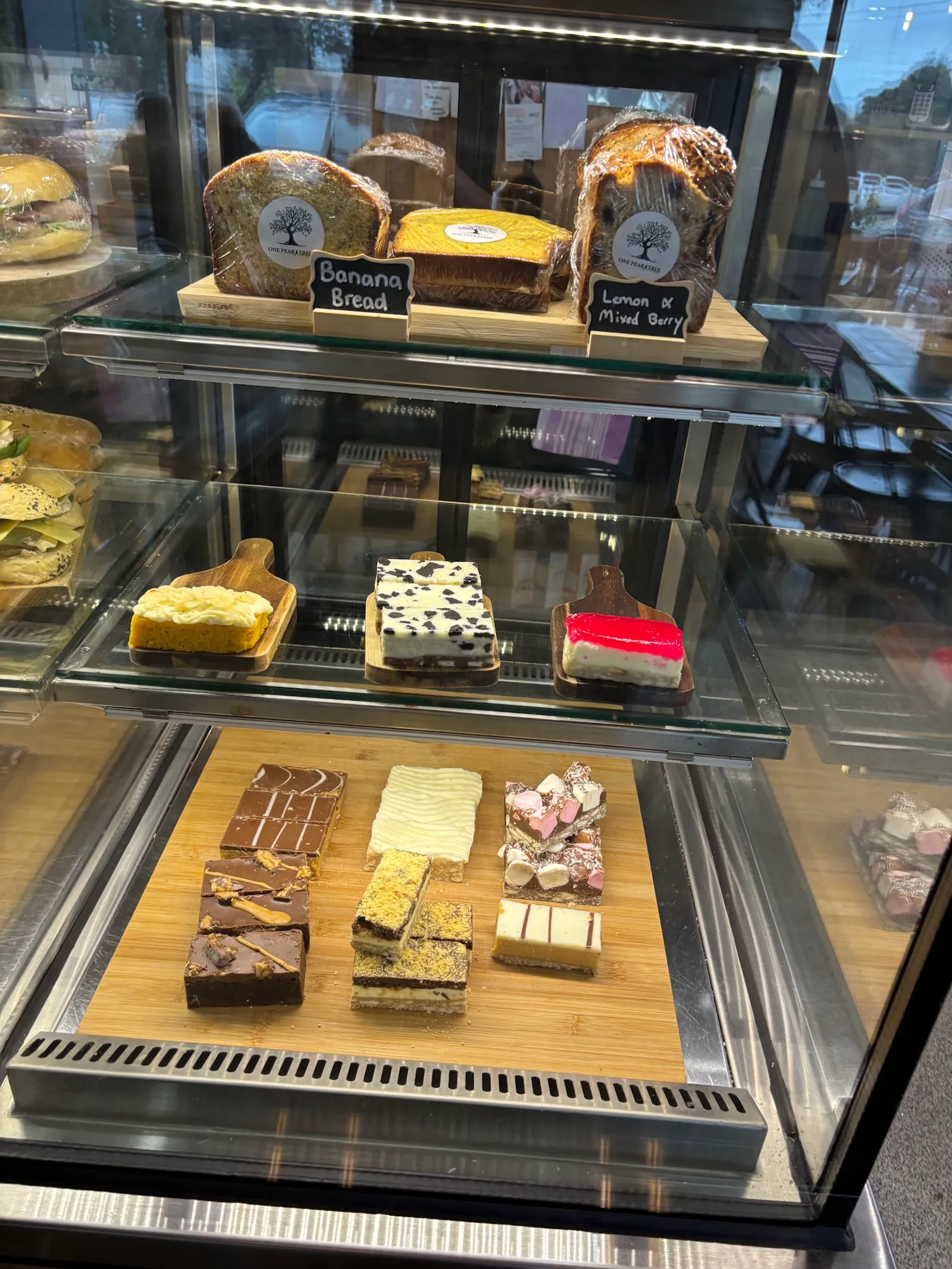 Three-shelf glass display cabinet with banana bread, cakes and assorted slices