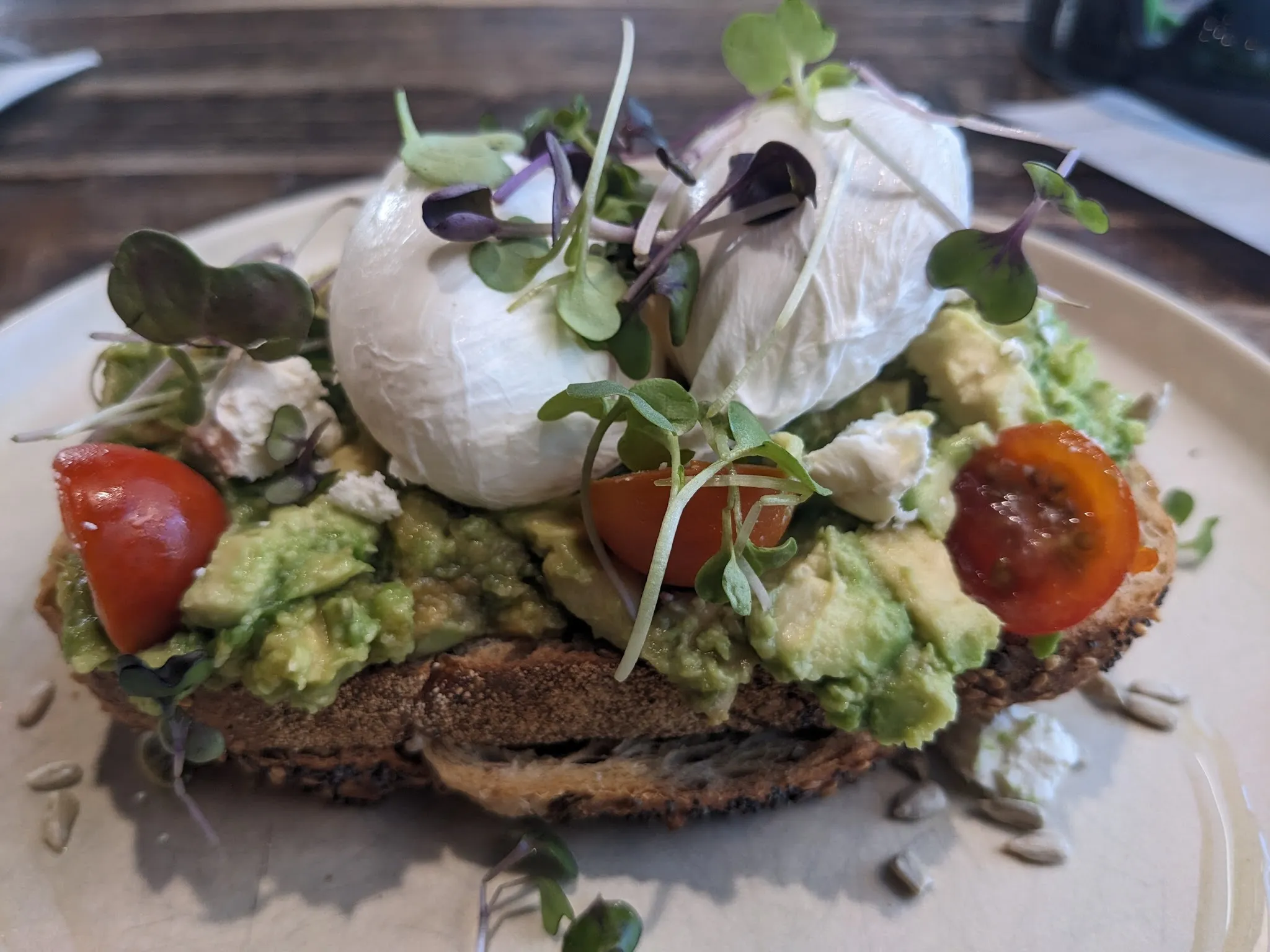 Avocado toast with two poached eggs, edible flower and microgreens on beige ceramic plate