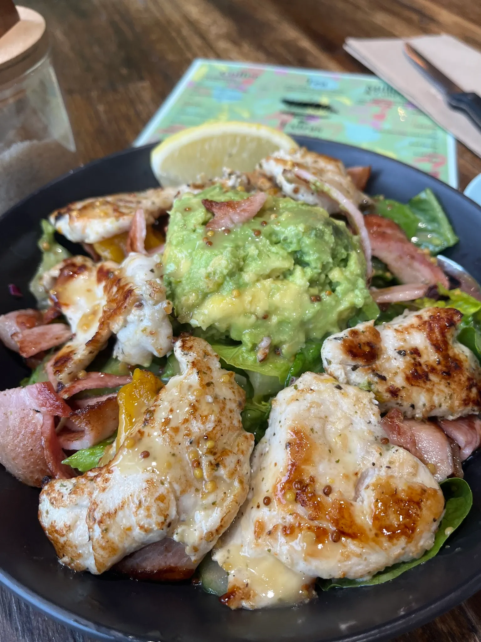 Grilled chicken salad with guacamole, bacon and capsicum in a dark skillet