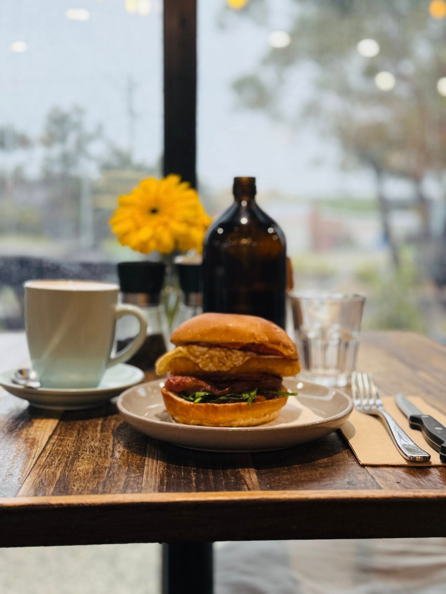 Breakfast burger and coffee at a window table with yellow flower and bokeh fairy lights behind