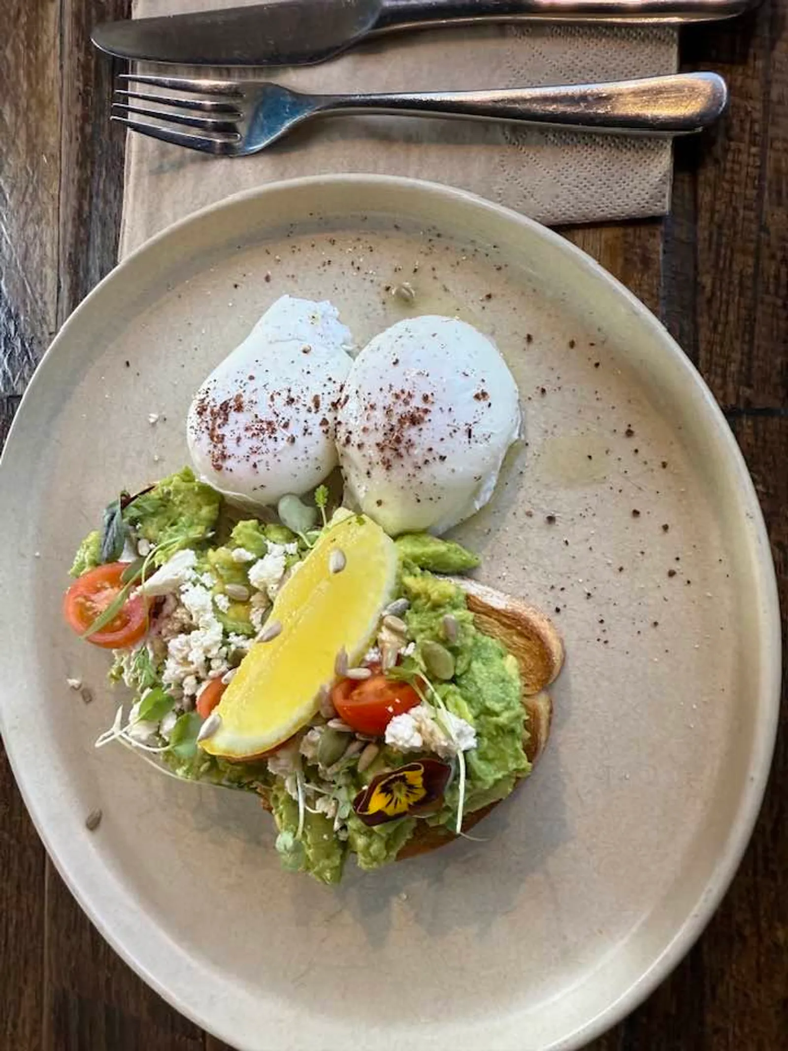 Avocado toast with two poached eggs, edible flowers and microgreens on oval ceramic plate